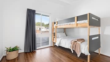 A bunk bed in a room with a sliding door, a potted plant, and wooden flooring.