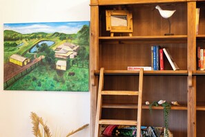 A bookshelf with books and decorative items, a framed painting of a landscape, and a wooden ladder.