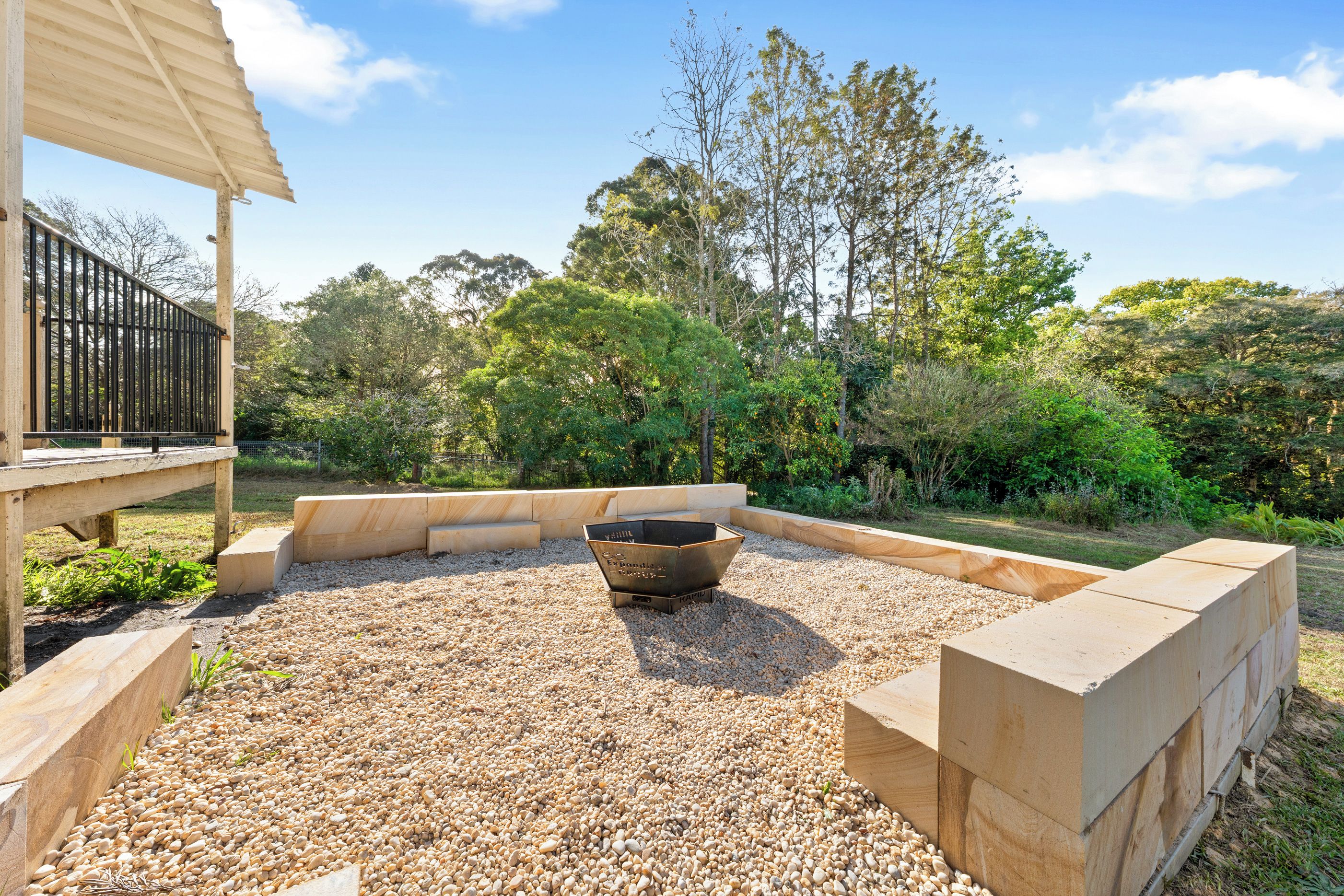 A landscaped outdoor area with a fire pit, wooden deck, and surrounding vegetation.