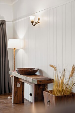Una mesa de madera con un cuenco y una lámpara, una lámpara de pared y una maceta con plantas secas.