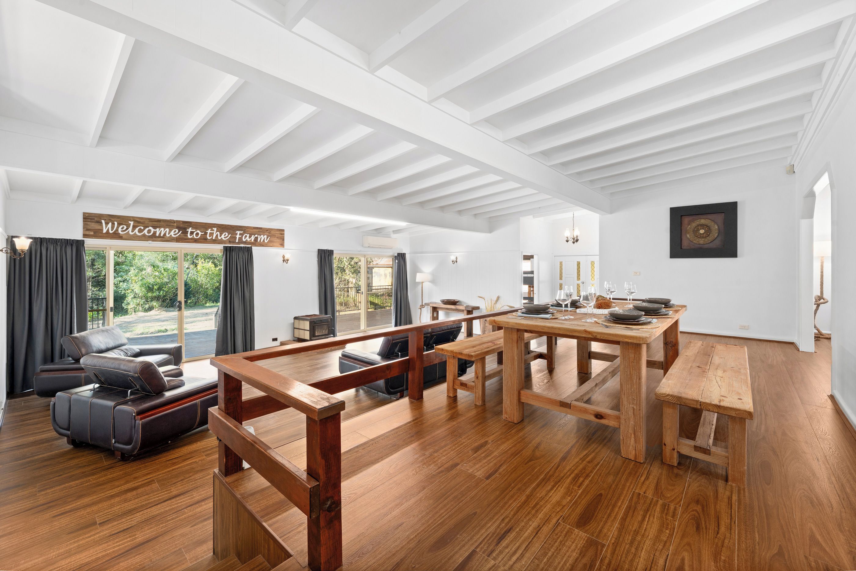 A spacious room with a wooden dining table, a sofa, and a bench. A sign reads 'Welcome to the Farm.'