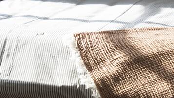 Una cama con cabecera de madera, almohada a rayas y manta con textura.