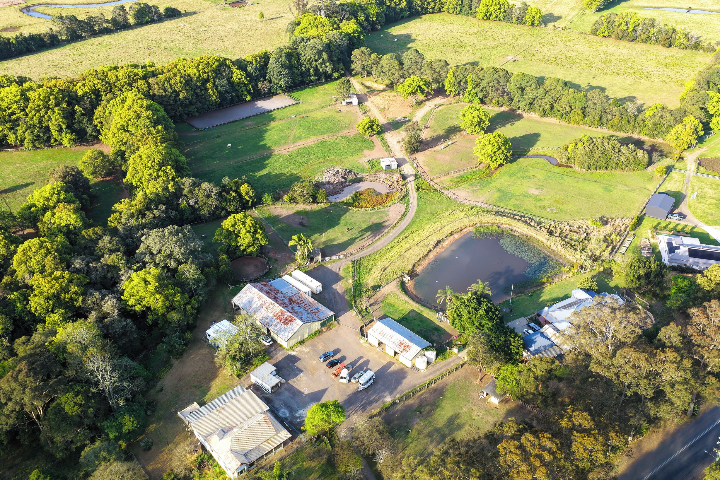 An aerial view of a rural property with multiple buildings, a pond, and surrounding fields.