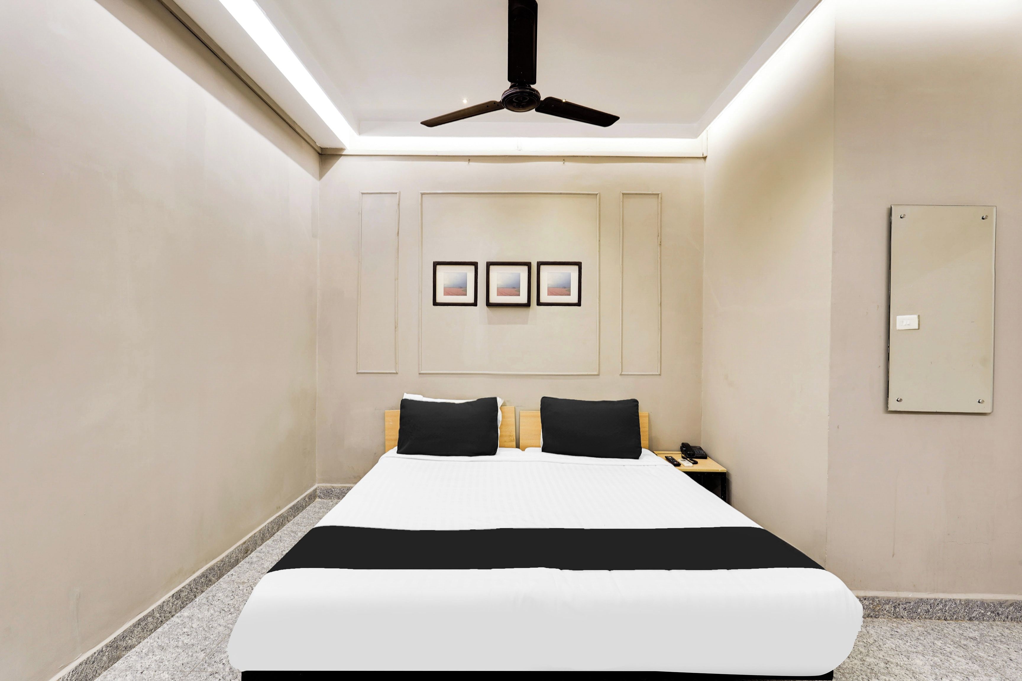 Una camera d'hotel con un letto, una ventola a soffitto, un comodino con un telefono e tre quadri appesi al muro.
