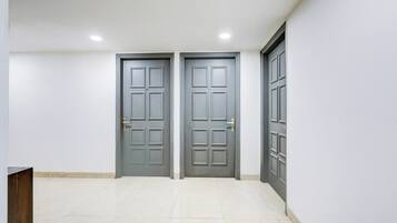 Corredor com duas portas cinzas, cada uma com uma placa de identificação, e chão de azulejos brancos.