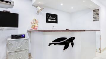 A reception desk with a sign indicating it's a company-serviced collection point, a wall-mounted air conditioning unit, a flat-screen TV, and a decorative statue.