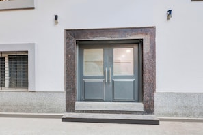 A building entrance with a double door, a small step leading up to it, and a window with a metal grille to the left.