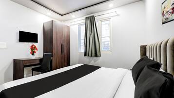 Quarto de hotel com cama, escrivaninha, cadeira, televisão e janela com cortinas.
