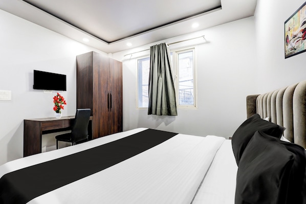 A hotel room with a bed, a desk, a chair, a television, and a window with curtains.