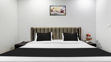 A hotel room with a bed, a nightstand, a phone, a painting on the wall, and a vase with flowers.