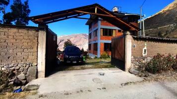 A building with a car parked in front, a stone wall on the left, and a mountain in the background.