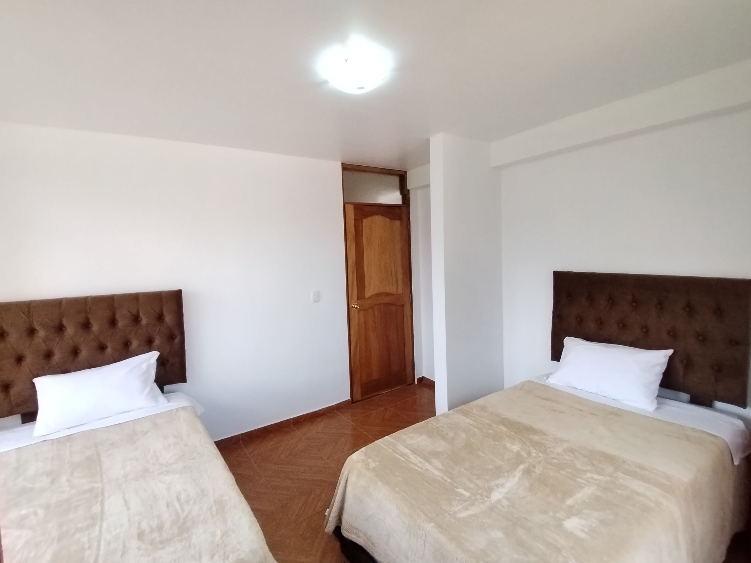 Une chambre d’hôtel avec deux lits, chacun doté d’une tête de lit marron et de draps blancs. Une porte en bois se trouve au centre de la pièce.