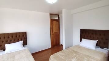 Une chambre d’hôtel avec deux lits, chacun doté d’une tête de lit marron et de draps blancs. Une porte en bois se trouve au centre de la pièce.