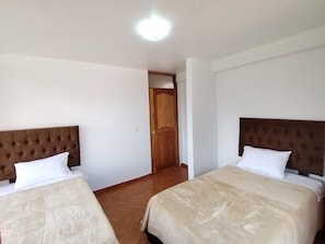 Une chambre d’hôtel avec deux lits, chacun doté d’une tête de lit marron et de draps blancs. Une porte en bois se trouve au centre de la pièce.