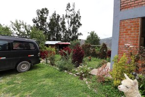 Un vehículo estacionado en un jardín, con un edificio y árboles al fondo.
