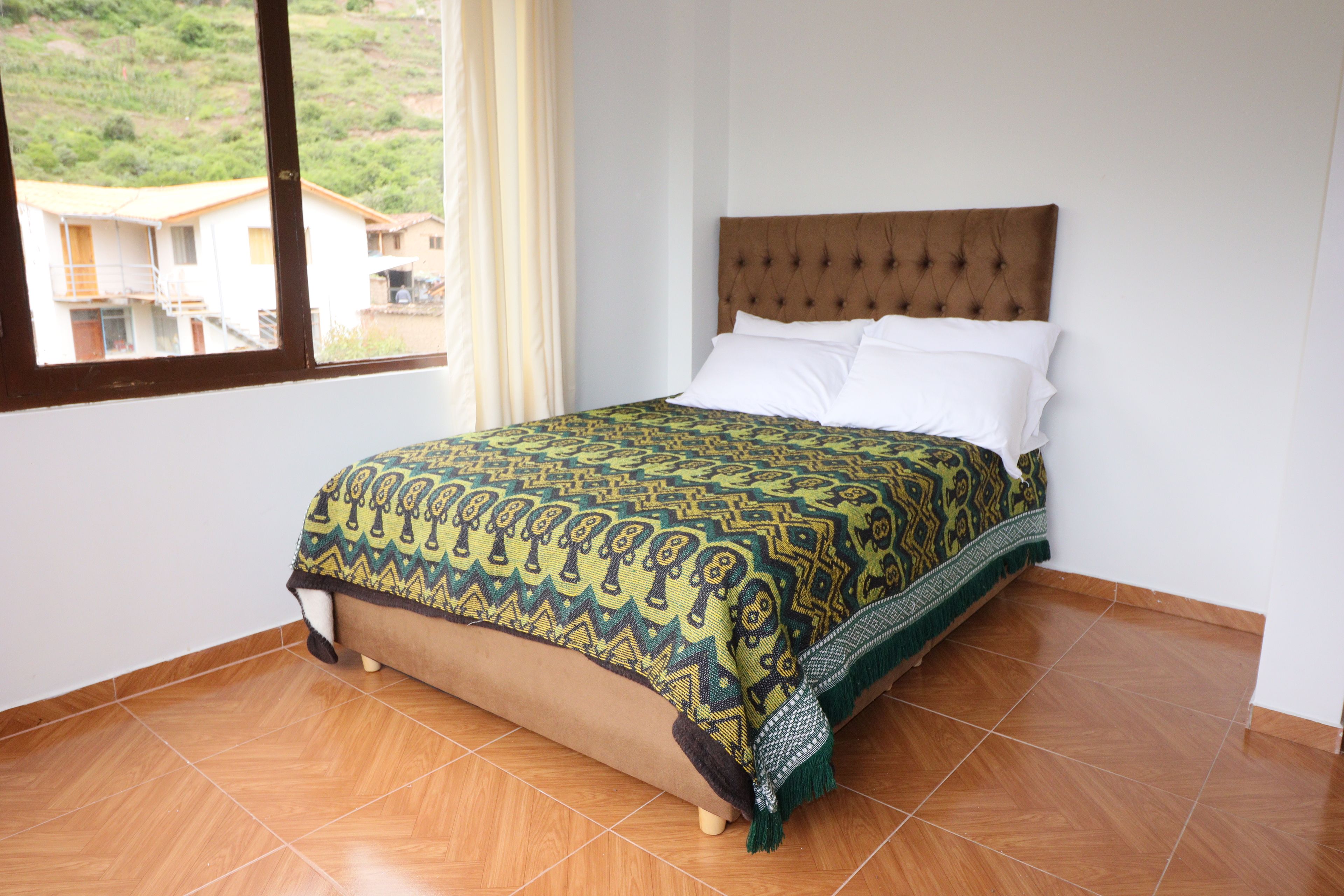 Un dormitorio con cama, ventana y vistas a edificios.