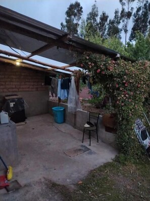 Un espacio al aire libre techado con un muro de ladrillo, un contenedor de plástico azul y una silla.