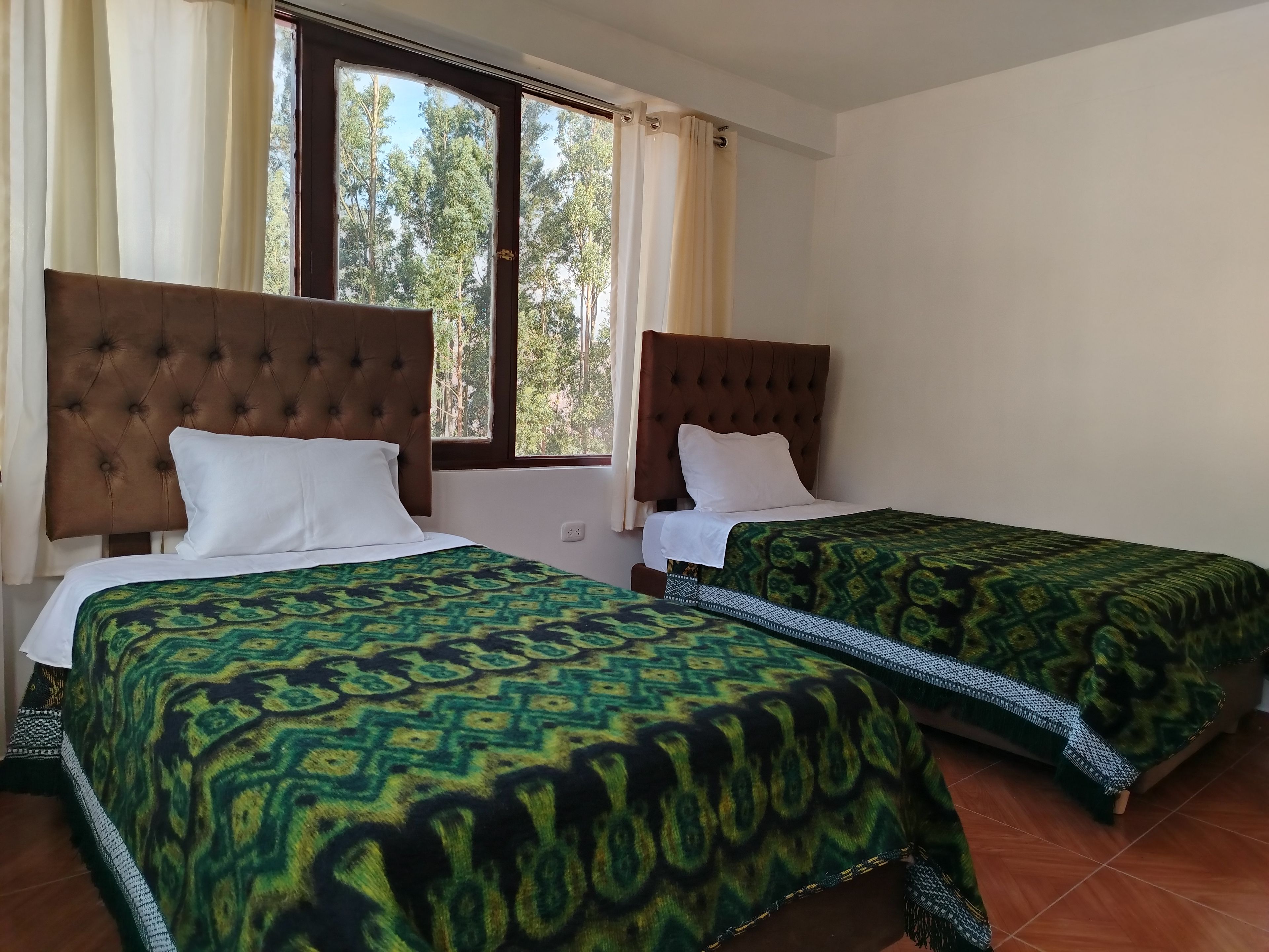 Habitación de hotel con dos camas, cada una con cabecera capitonada, colcha estampada y ventana con cortinas.