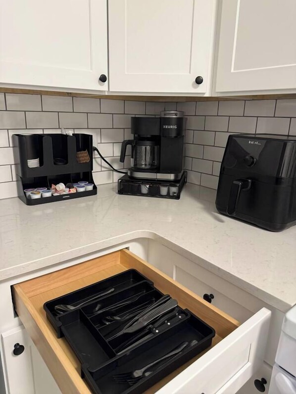 A kitchen with white cabinets, a coffee maker, and a drawer organizer.