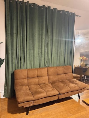 A brown sofa in a room with a green curtain.