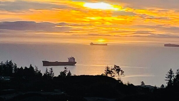 Een zonsondergang boven het water, met schepen en een bebost gebied op de voorgrond.