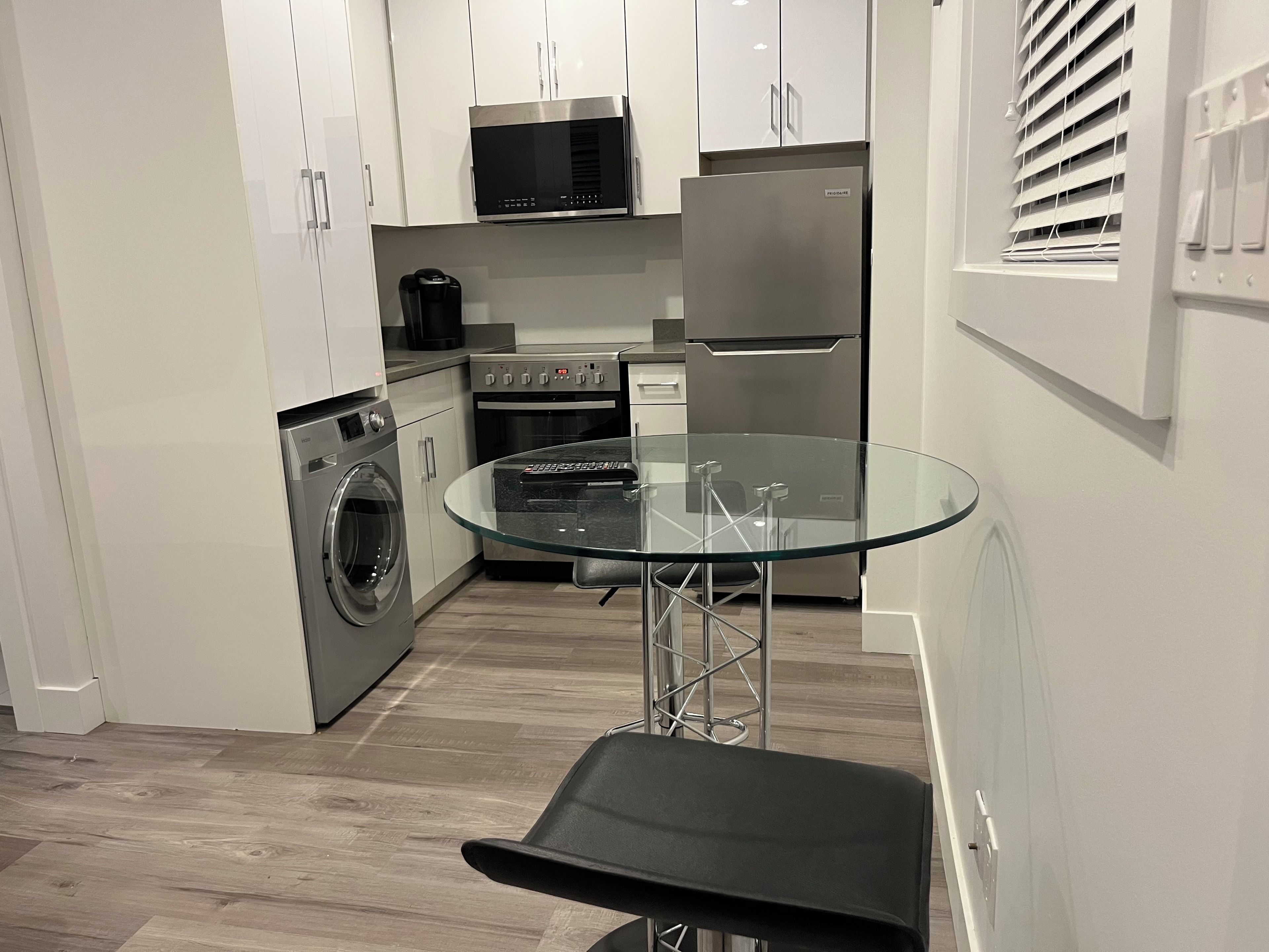 Cozinha moderna com eletrodomésticos de aço inoxidável, mesa com bancada de vidro e máquina de lavar embutida.