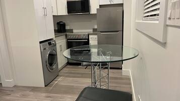 Cozinha moderna com eletrodomésticos de aço inoxidável, mesa com bancada de vidro e máquina de lavar embutida.