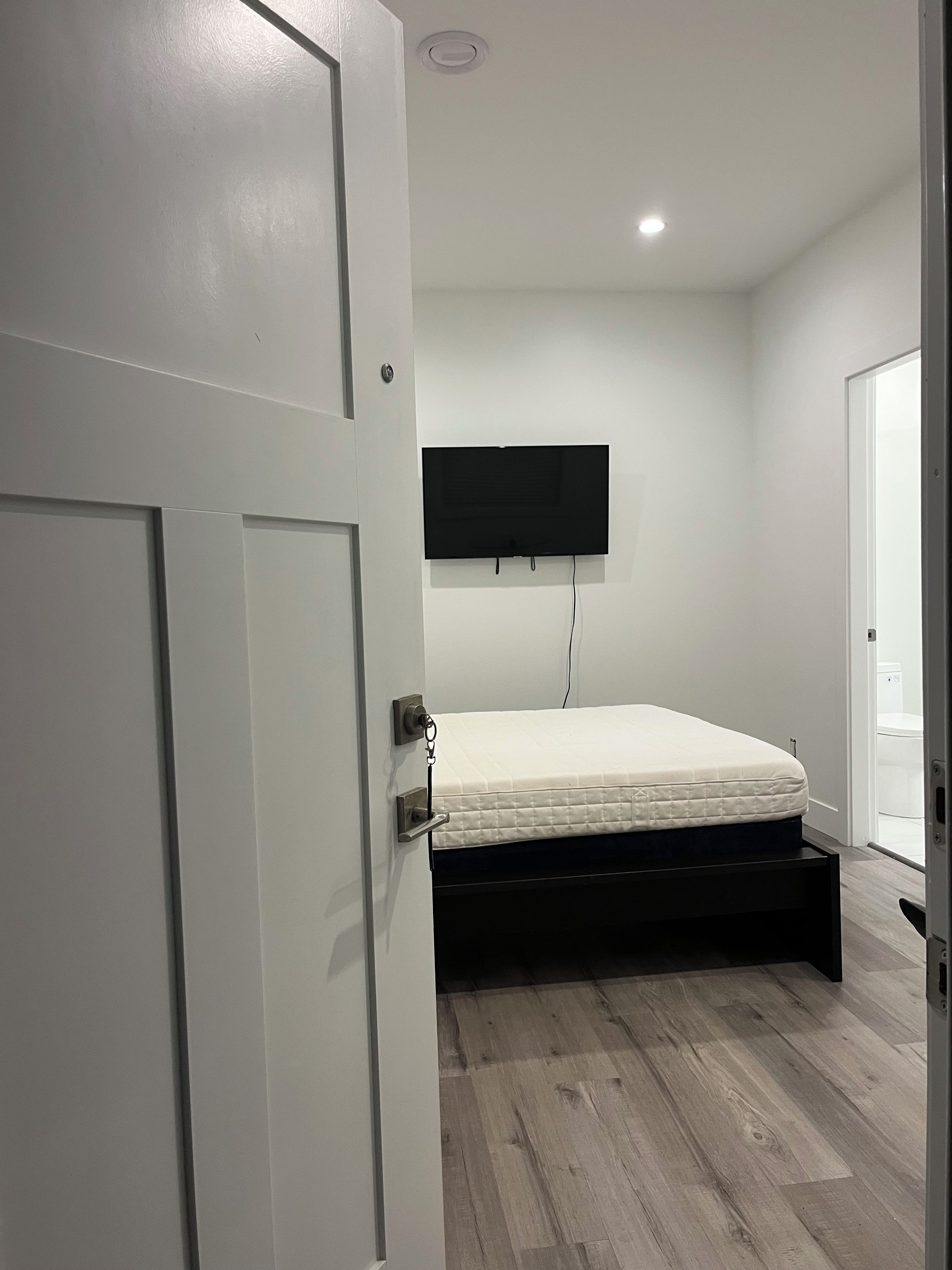 Une chambre à coucher avec un lit, un téléviseur fixé au mur et une porte.