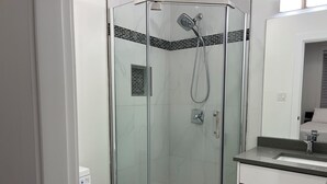 Een moderne badkamer met een douche met glazen wand, een toilet en een wastafel met spiegel.