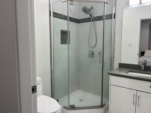 Moderni kylpyhuone, jossa on lasiseinällä varustettu suihku, wc ja peilillä varustettu pesuallas.