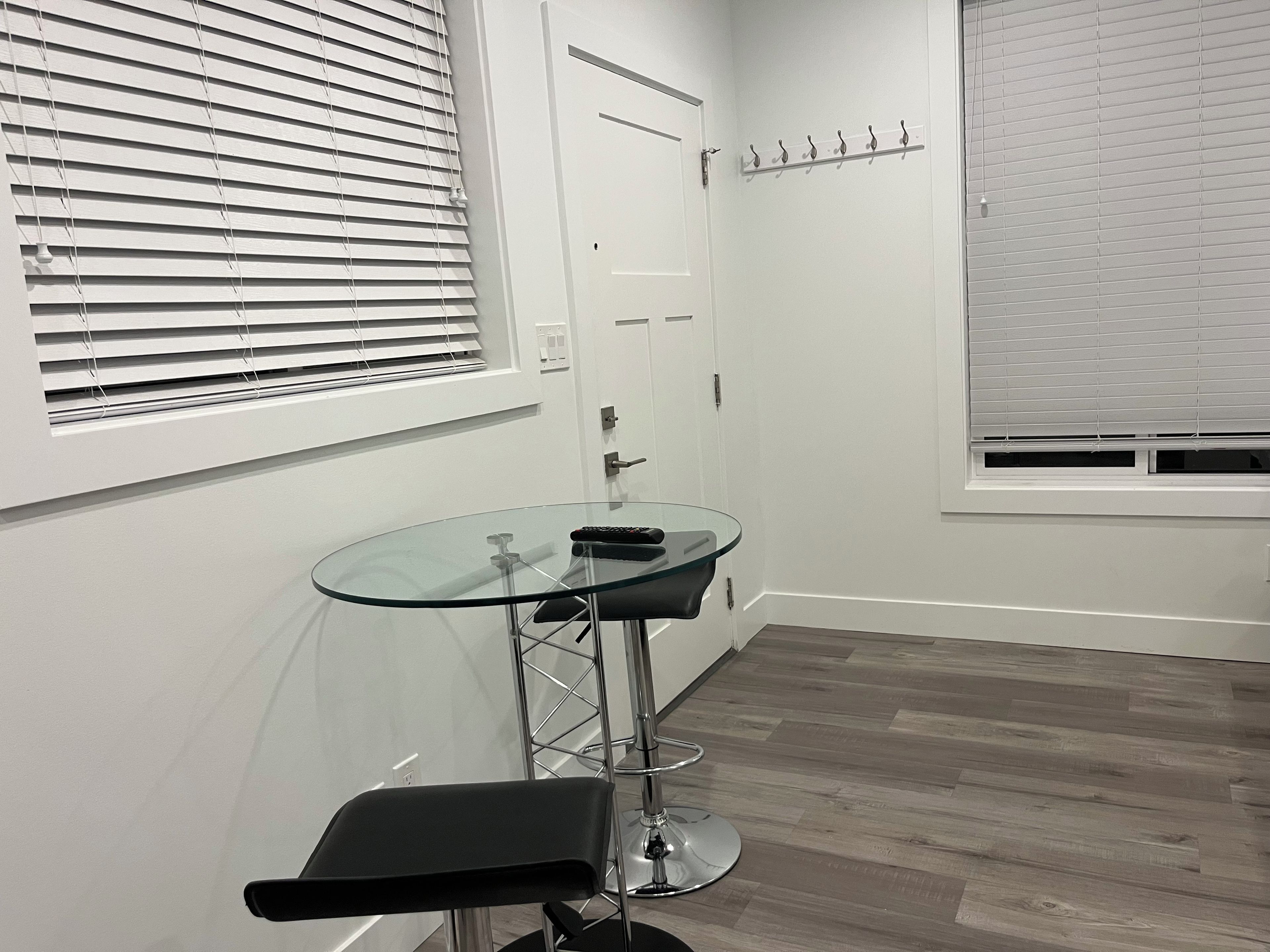 Une pièce comprenant une table avec un plateau en verre, une chaise noire, une porte et un porte-manteau.
