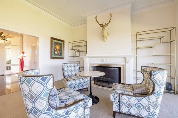 A spacious living room with patterned chairs, a fireplace, and a mounted deer head.