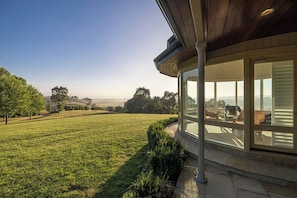 A modern house with a large glass window overlooking a grassy field.