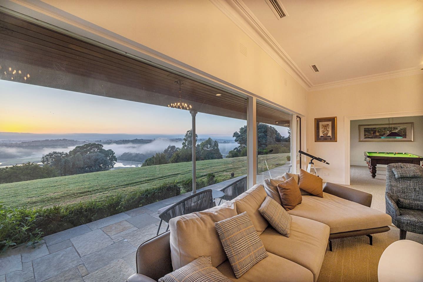 A modern living room with a large window overlooking a scenic landscape, a pool table, and a comfortable seating area.