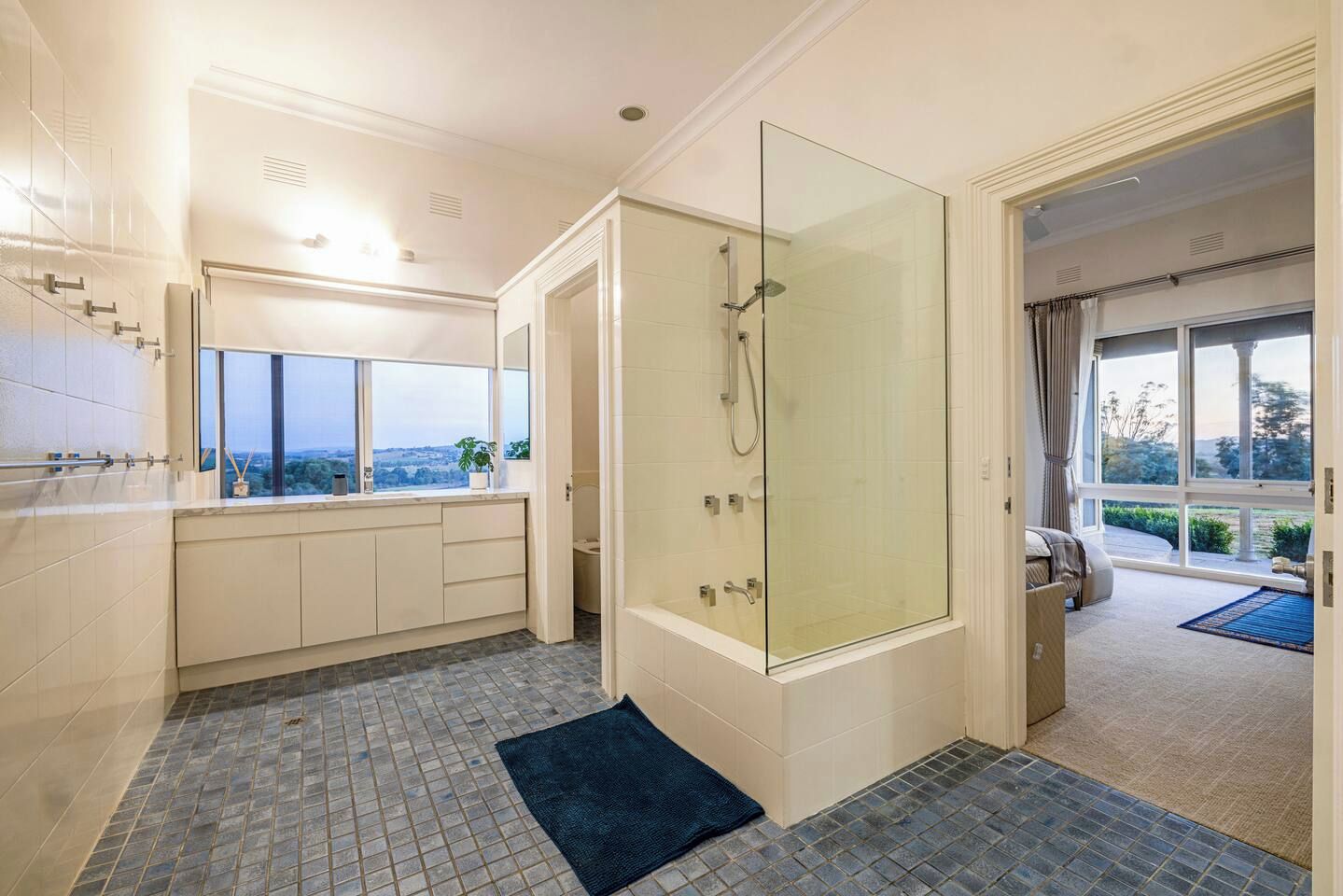 Ein modernes Badezimmer mit einer gläsernen Dusche, einem großen Fenster und Blick ins Freie.