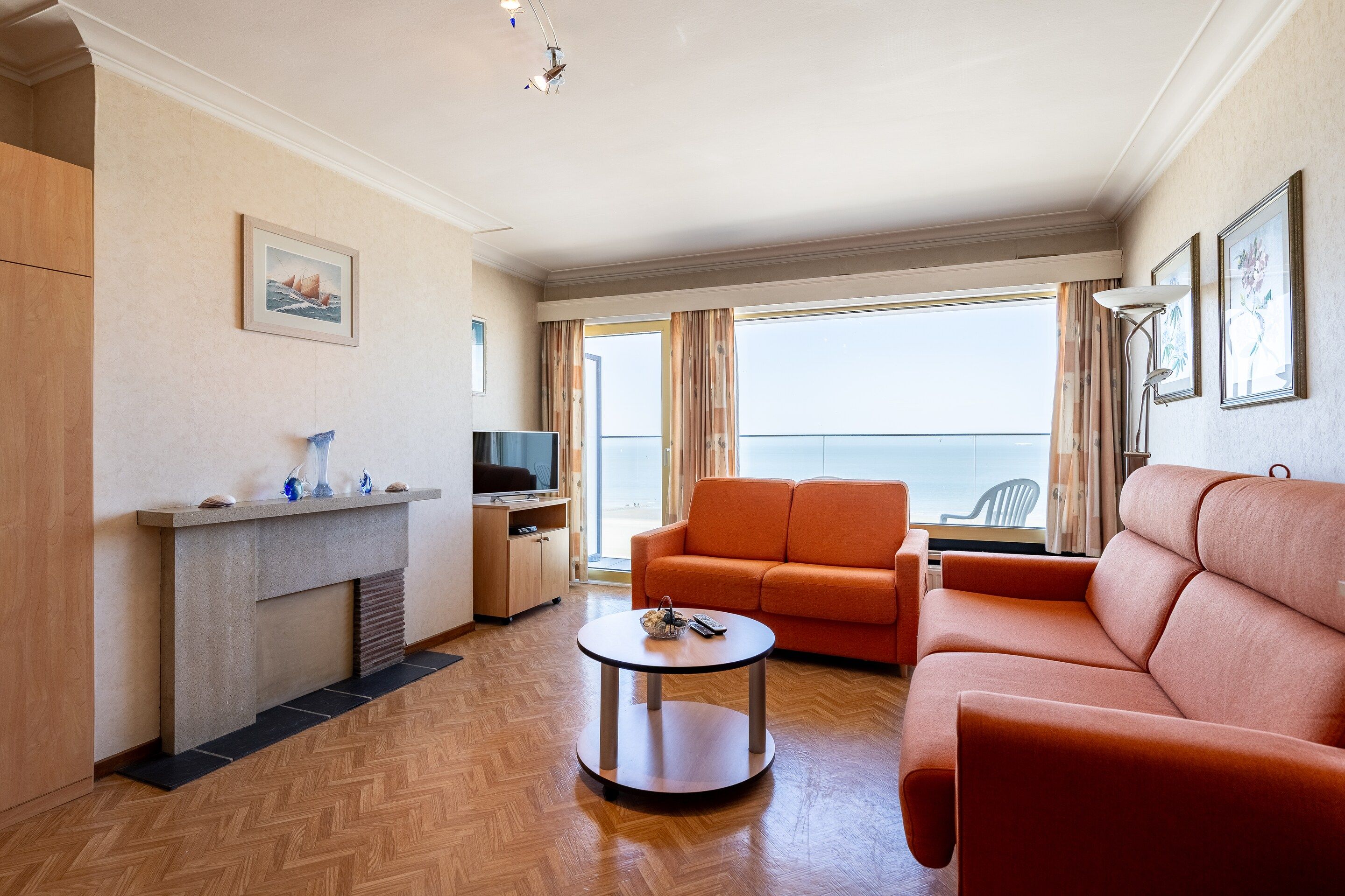 A hotel room with a sofa, armchair, TV, fireplace, and a balcony with a view.