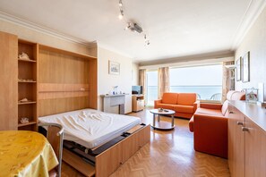 A hotel room with a bed, a sofa, a small table, a TV, and a window with a view. - Studio in Zeedijk With Stunning Sea Views (Blankenberge)