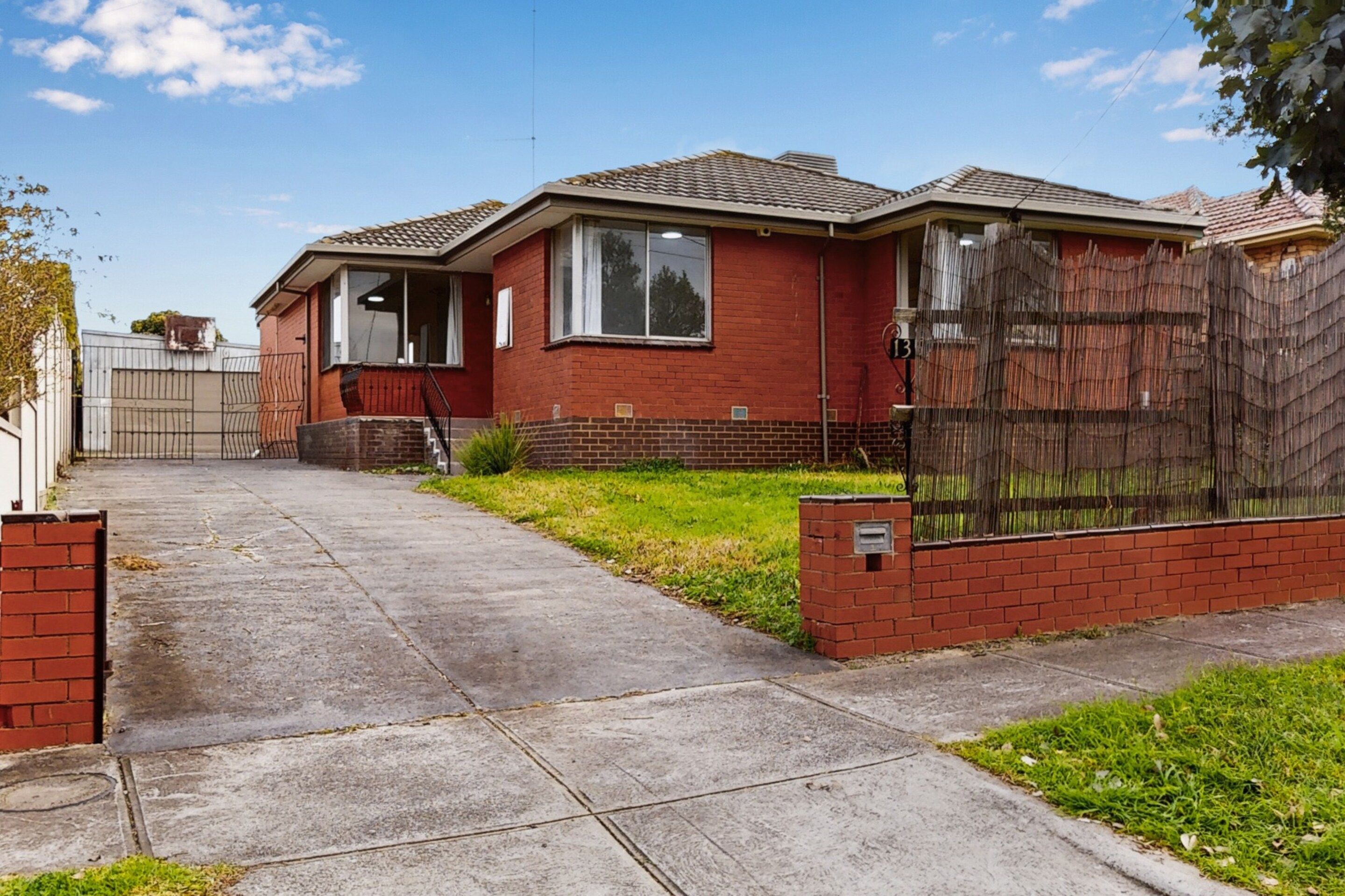A two-story brick house with a front yard, a metal gate, and a wooden fence.