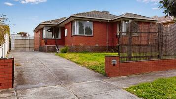 A two-story brick house with a front yard, a metal gate, and a wooden fence.