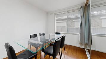 A room with a glass-top table and black chairs, a window with blinds, and wooden flooring.