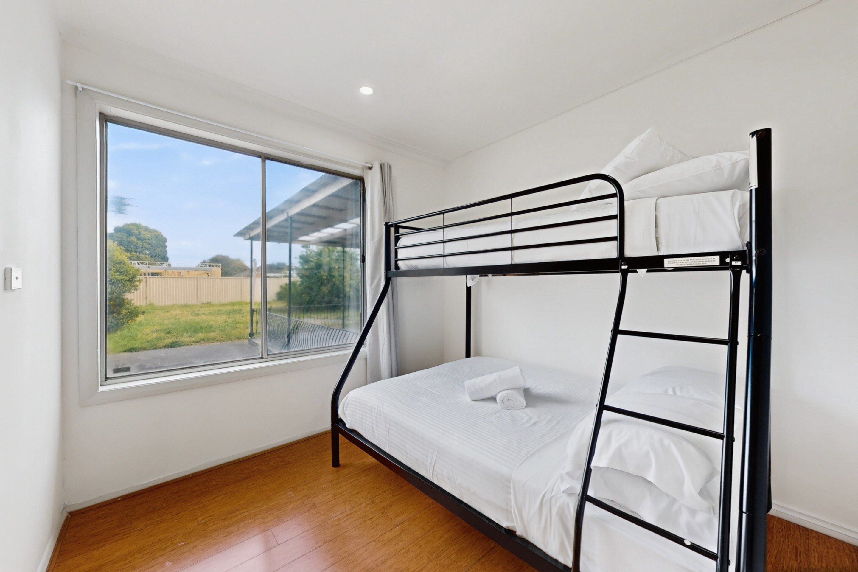 A bunk bed in a room with a large window, wooden flooring, and white walls.