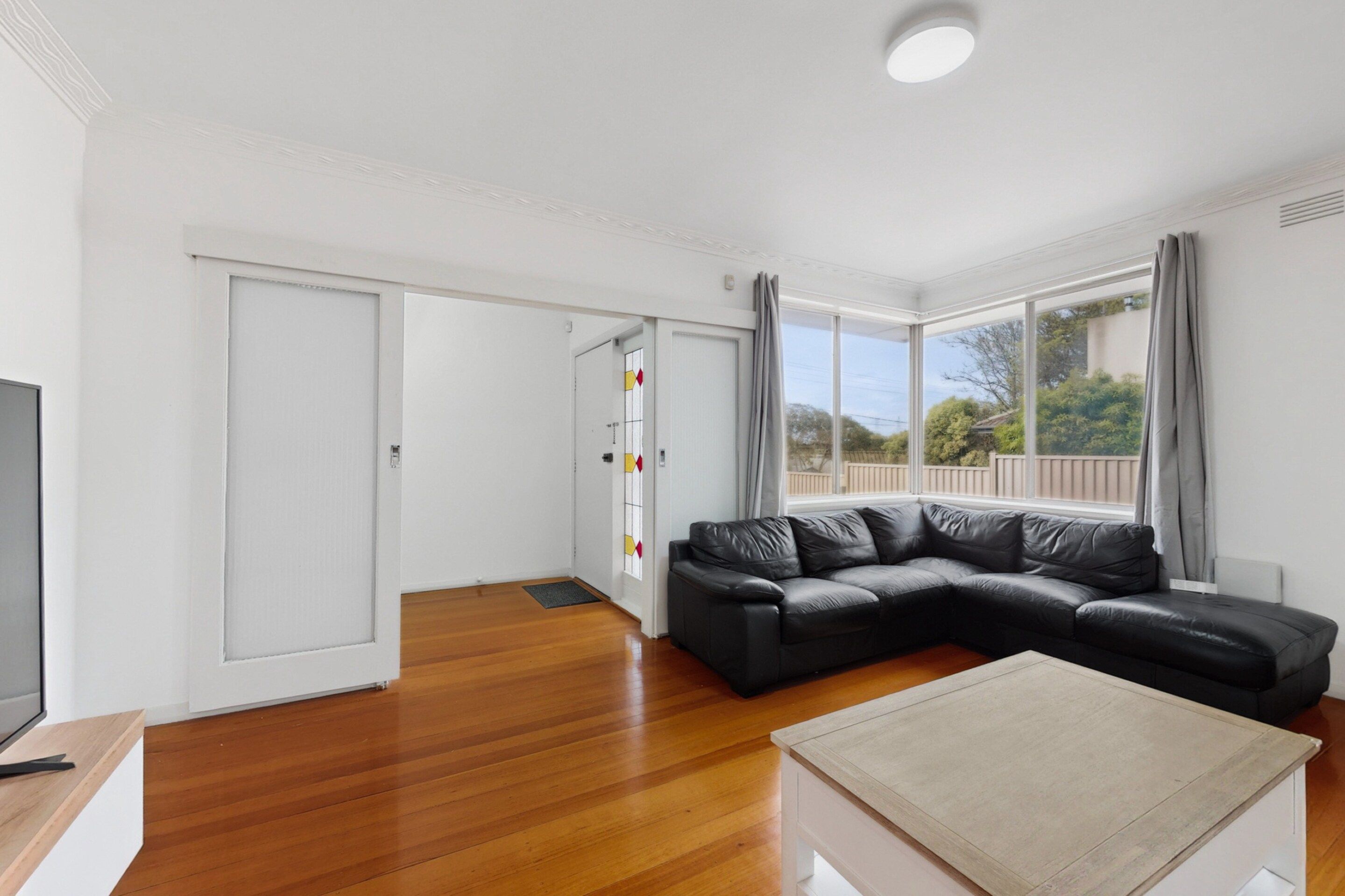 A modern living room with a black leather sofa, a wooden coffee table, and a TV on a wooden stand.