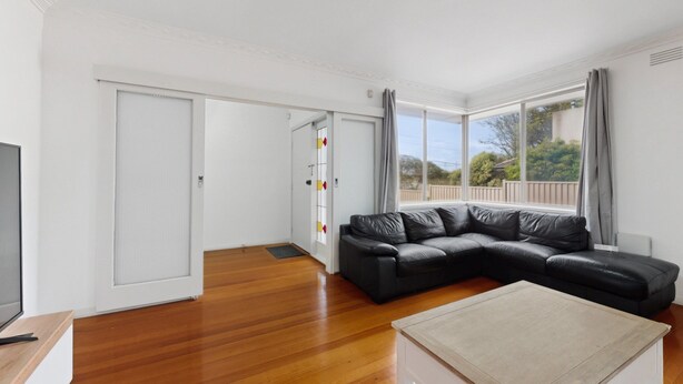 A modern living room with a black leather sofa, a wooden coffee table, and a TV on a wooden stand. - Spacious 4-bed House With Garden in Glenroy (Melbourne)