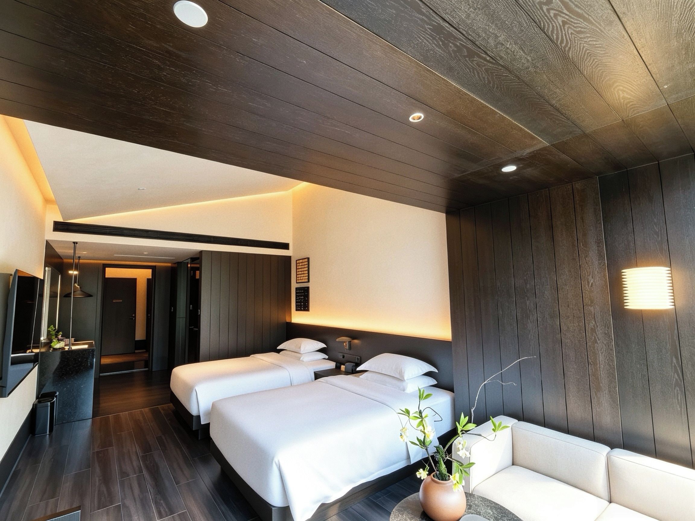 Ein modernes Hotelzimmer mit zwei Betten, einer Couch, einer Topfpflanze und einer wandmontierten Bedienkonsole.