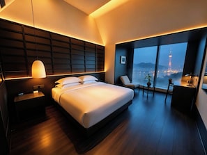 Una habitación de hotel moderna con una cama grande, zona de estar y vistas a un paisaje urbano.