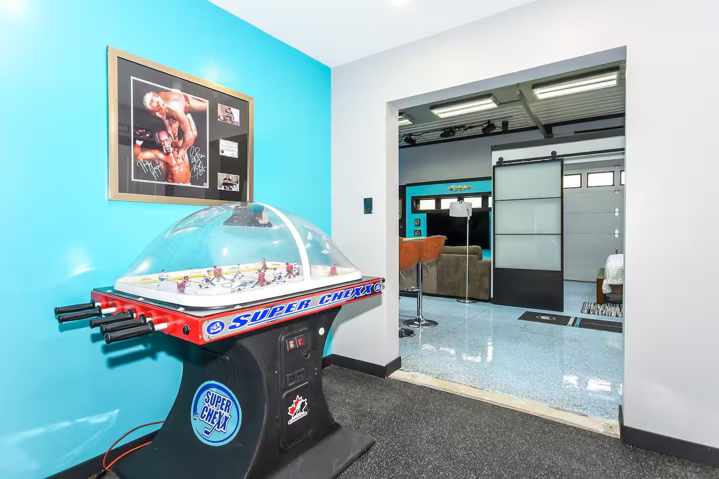 Une pièce avec une table de baby-foot, une photo encadrée au mur et un coin bar avec des tabourets.