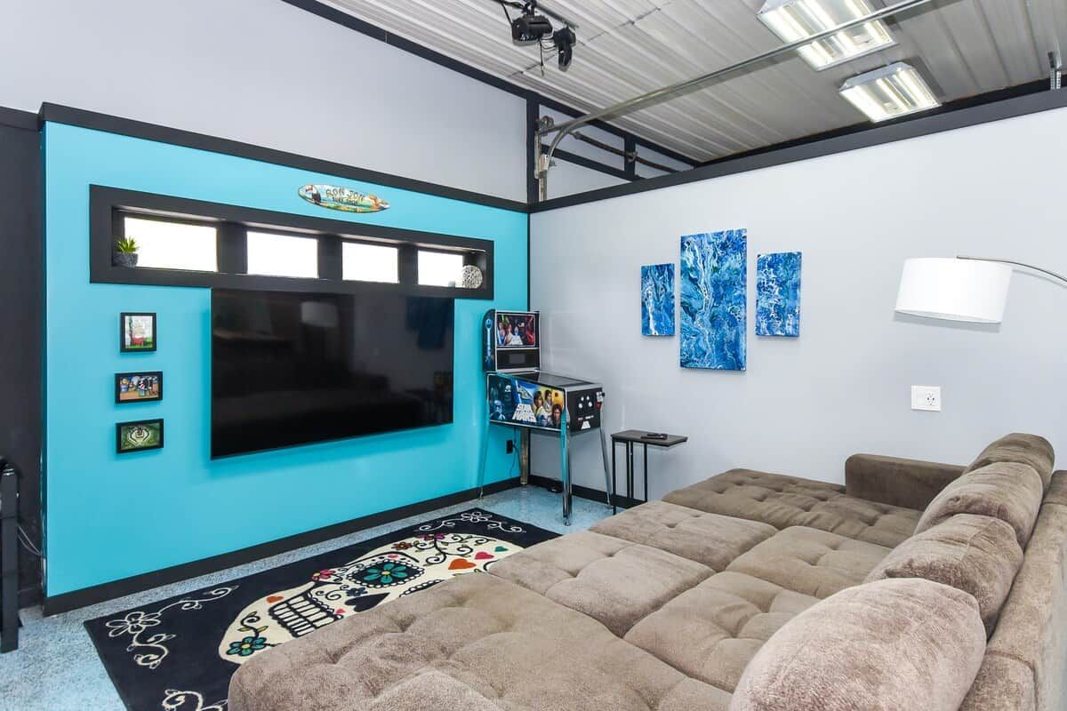 A room with a large flat-screen TV, a blue accent wall, a brown sofa, and a patterned rug.