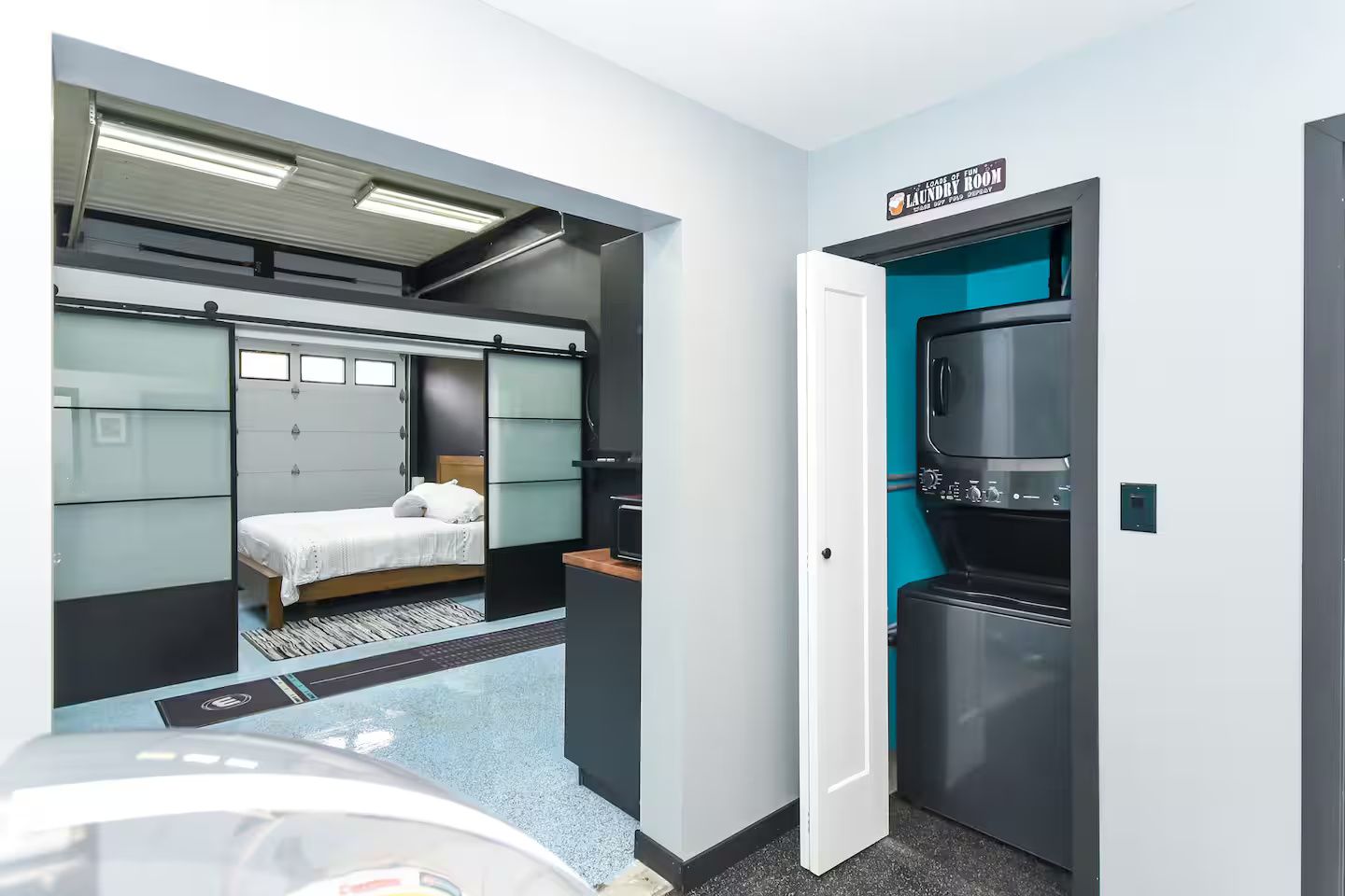 A compact hotel room with a bed, a small desk, a minibar, and a laundry room sign.