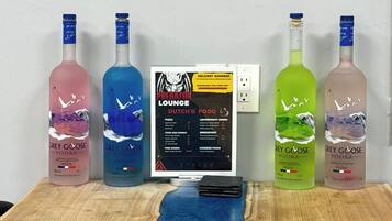 A room with a TV displaying a movie, a laptop, and four bottles of Grey Goose vodka on a wooden table.