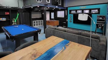 A pool table with a blue felt surface, a grey sofa, and a wooden table with a blue stripe.